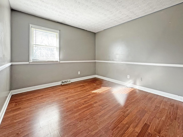 unfurnished room with wood finished floors, visible vents, and baseboards