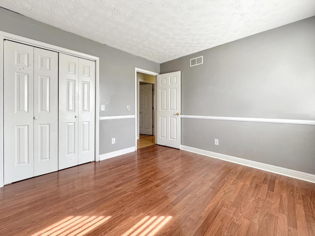 unfurnished bedroom featuring a closet, visible vents, a textured ceiling, wood finished floors, and baseboards