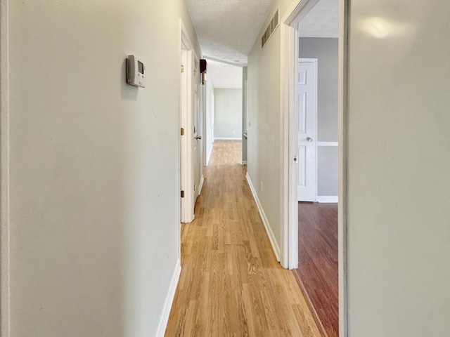 corridor featuring light wood-style floors, baseboards, visible vents, and a textured ceiling