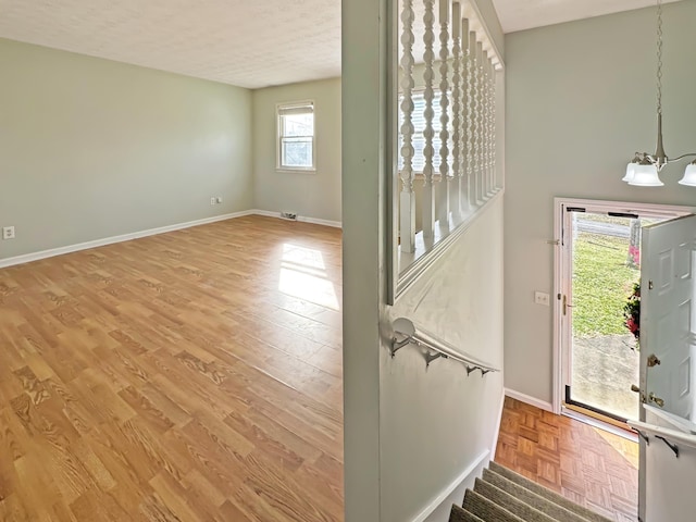 interior space featuring a textured ceiling, an inviting chandelier, parquet flooring, and baseboards