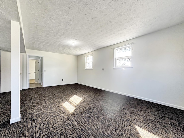 basement featuring a textured ceiling, dark carpet, and baseboards