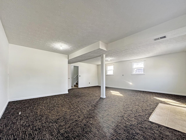 basement with a textured ceiling, visible vents, baseboards, stairs, and dark colored carpet