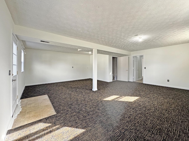 basement with baseboards, visible vents, dark carpet, and a textured ceiling