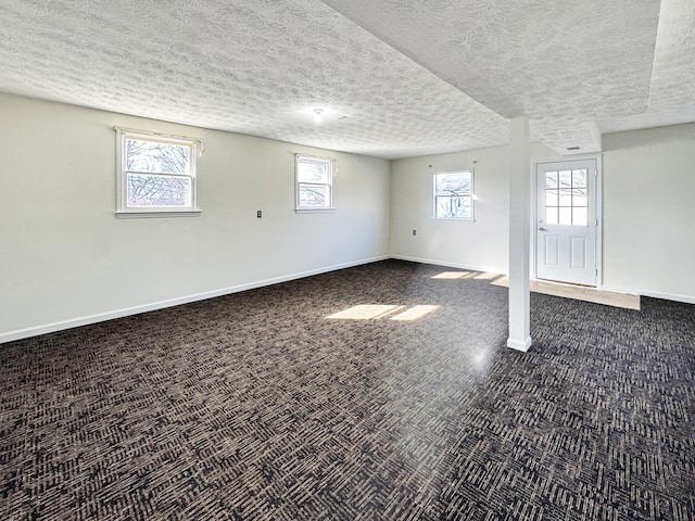 below grade area with dark colored carpet, a textured ceiling, and baseboards