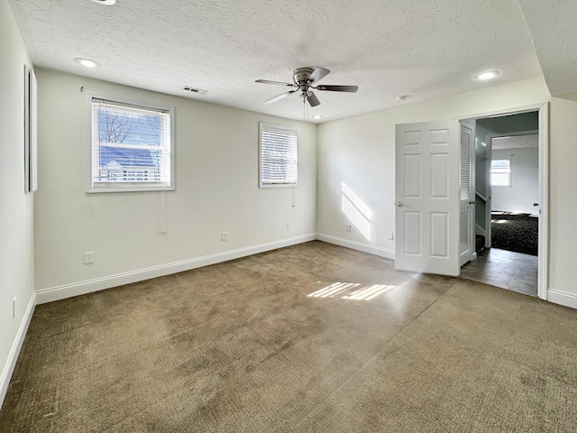 unfurnished bedroom featuring a textured ceiling, multiple windows, visible vents, and carpet flooring