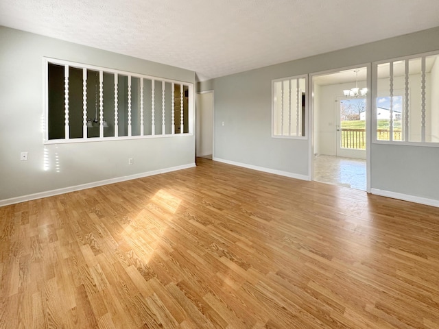 unfurnished room with a chandelier, a textured ceiling, baseboards, and wood finished floors