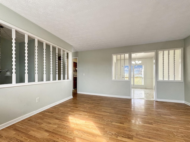 unfurnished room featuring baseboards, a textured ceiling, wood finished floors, and an inviting chandelier