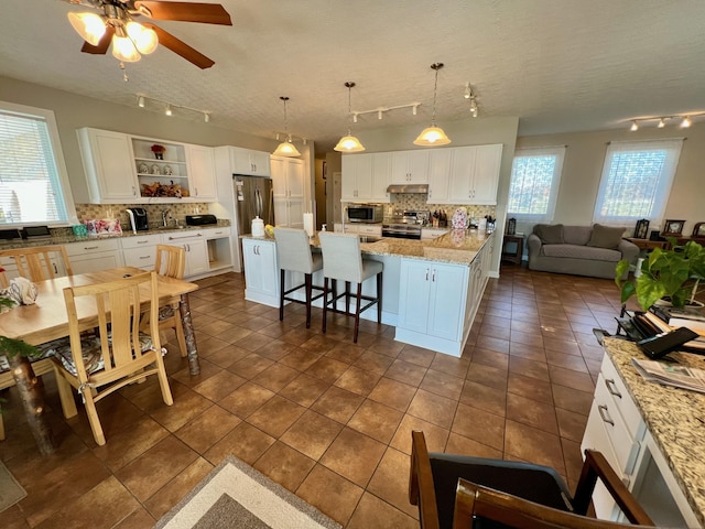 kitchen with a kitchen island, hanging light fixtures, stainless steel appliances, a kitchen bar, and white cabinetry