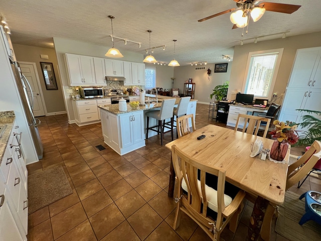 kitchen with light stone counters, pendant lighting, stainless steel appliances, white cabinetry, and an island with sink