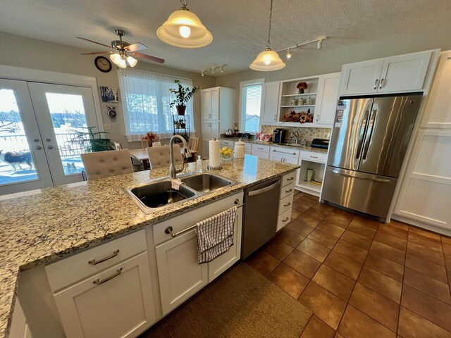 kitchen with light stone counters, stainless steel appliances, a sink, white cabinetry, and pendant lighting