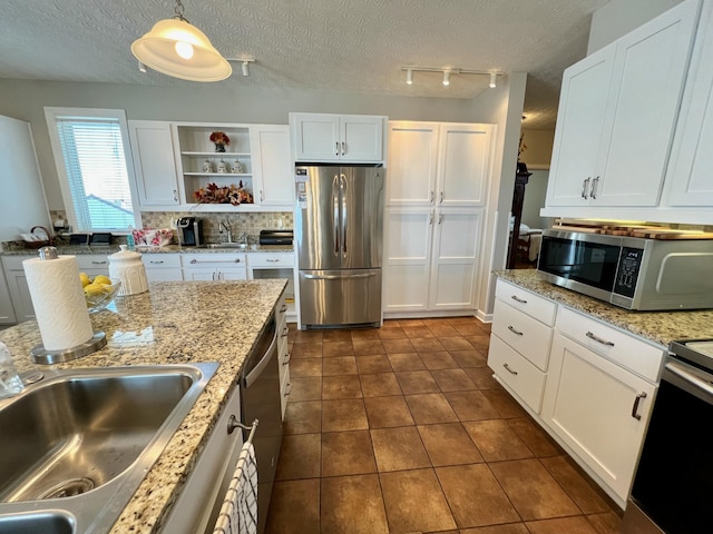 kitchen featuring stainless steel appliances, dark tile patterned floors, white cabinetry, pendant lighting, and a sink