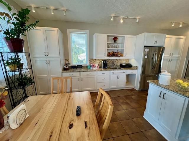 kitchen with freestanding refrigerator, light stone countertops, white cabinetry, open shelves, and a sink