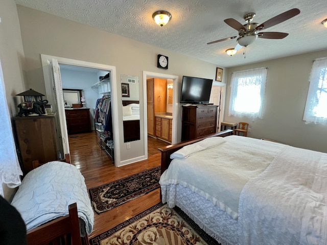 bedroom with a textured ceiling, ensuite bathroom, dark wood-type flooring, a spacious closet, and a closet