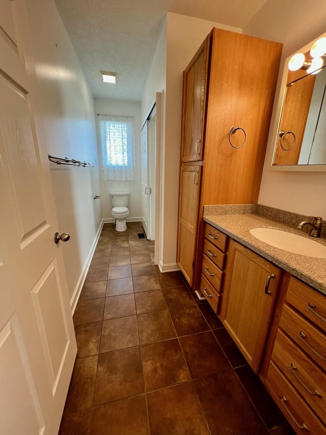 full bath with a textured ceiling, tile patterned flooring, toilet, vanity, and baseboards