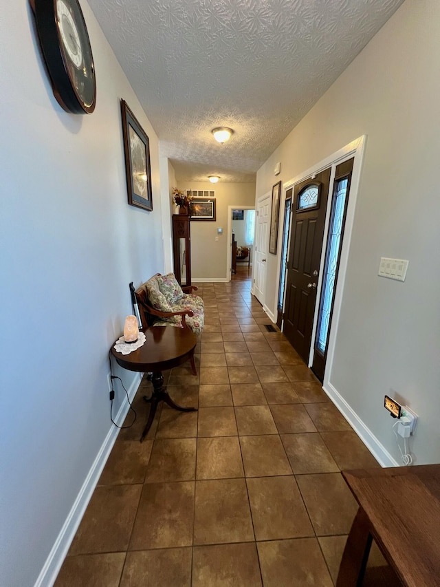 hall with baseboards, a textured ceiling, and dark tile patterned flooring