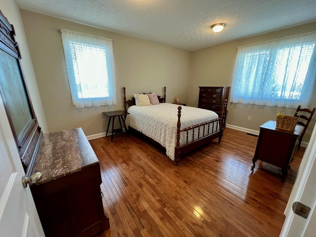 bedroom with visible vents, baseboards, dark wood finished floors, and a textured ceiling