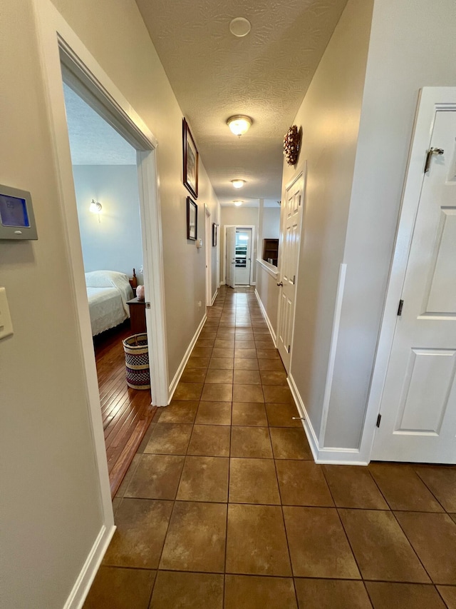 hallway featuring dark tile patterned flooring, a textured ceiling, and baseboards