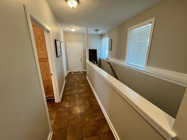 hall featuring an upstairs landing, baseboards, dark tile patterned floors, and a textured ceiling