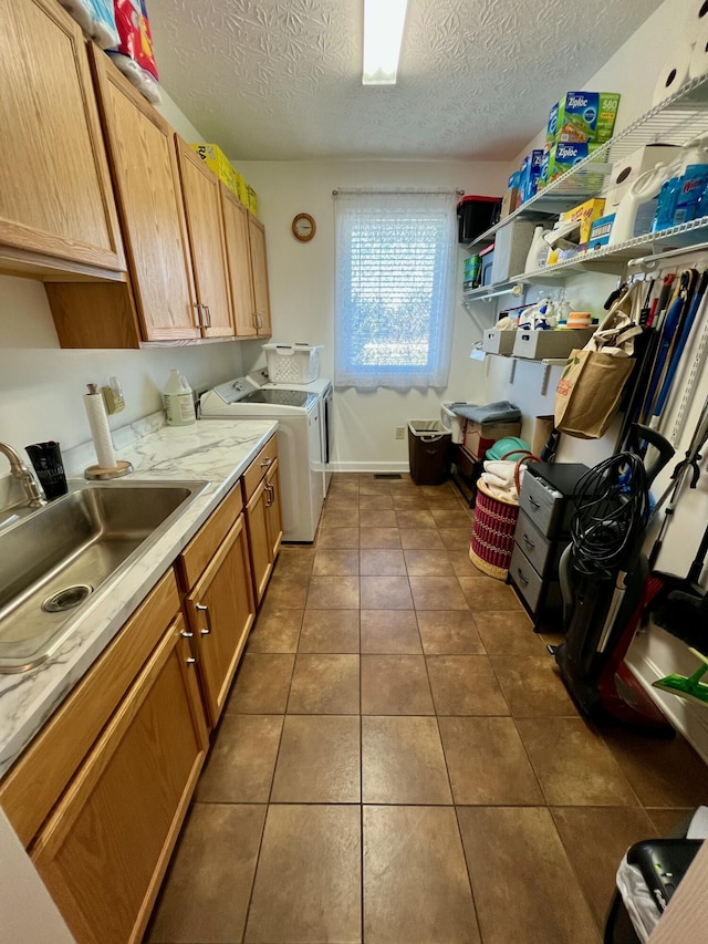 washroom featuring washing machine and clothes dryer, cabinet space, a sink, a textured ceiling, and dark tile patterned floors