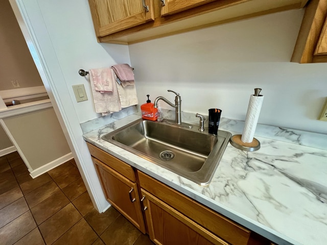 kitchen featuring light countertops, dark tile patterned floors, a sink, and brown cabinets