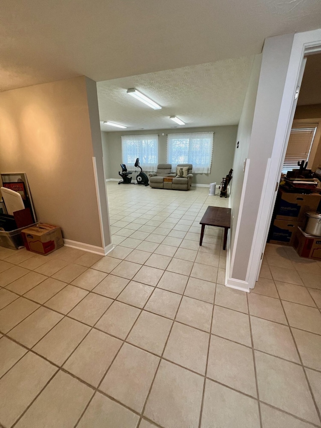 below grade area featuring light tile patterned floors, a textured ceiling, and baseboards