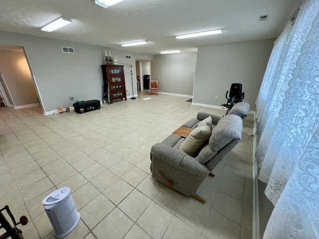 living room featuring baseboards, visible vents, a textured ceiling, and light tile patterned flooring