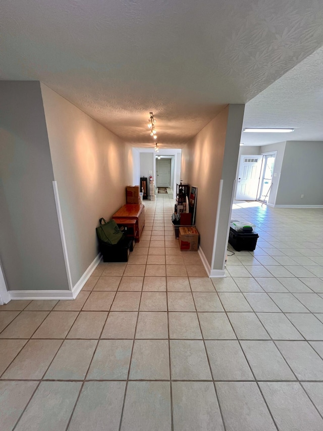 corridor featuring a textured ceiling, baseboards, and light tile patterned floors