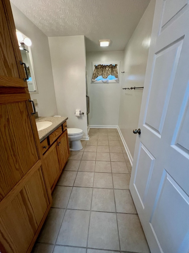 bathroom with a textured ceiling, tile patterned flooring, toilet, vanity, and baseboards