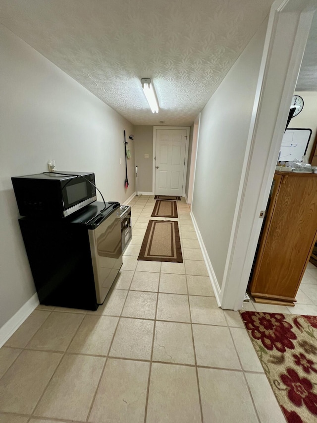 kitchen with brown cabinetry, a textured ceiling, baseboards, and light tile patterned floors