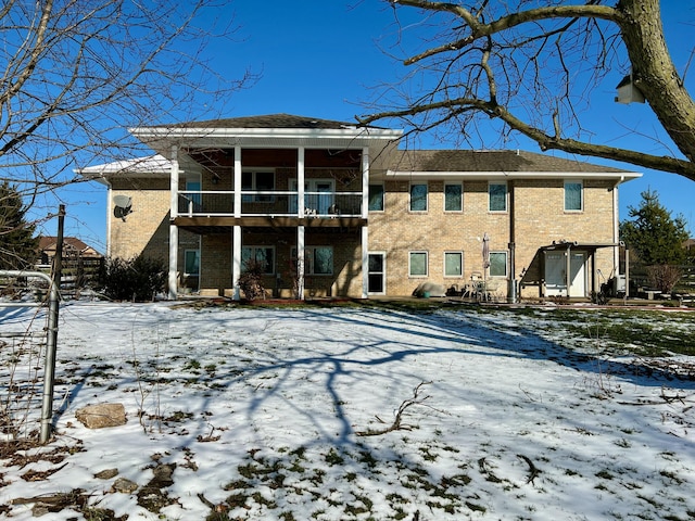 snow covered back of property featuring brick siding and a sunroom