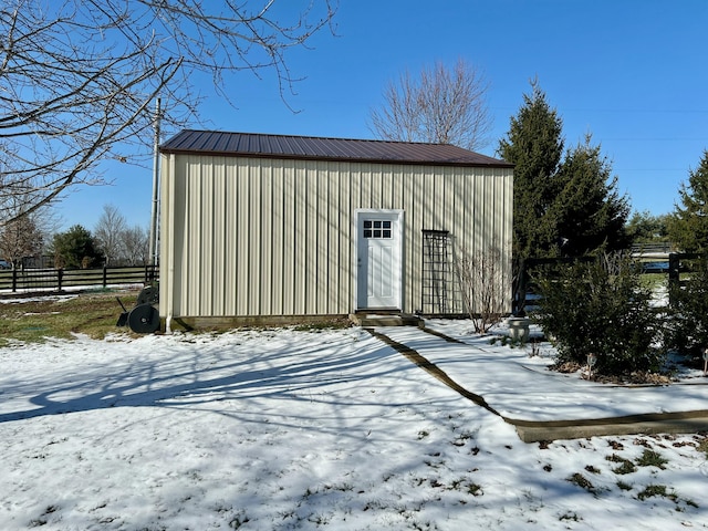 snow covered structure featuring fence and an outdoor structure