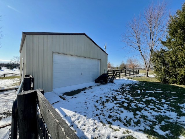 snow covered garage featuring a detached garage and fence