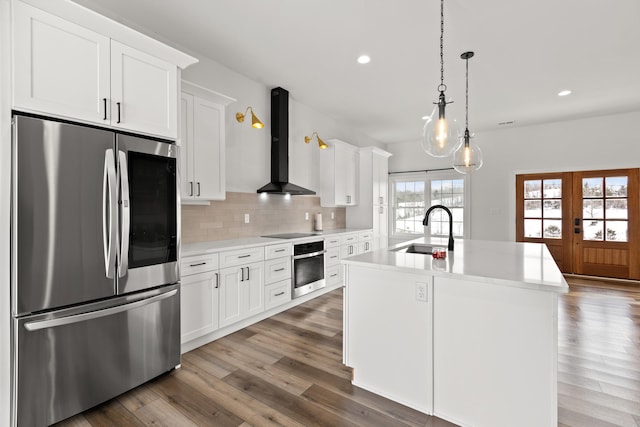 kitchen featuring a sink, light countertops, appliances with stainless steel finishes, wall chimney range hood, and a center island with sink