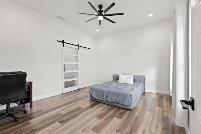 bedroom with light wood-style floors, a barn door, visible vents, and baseboards