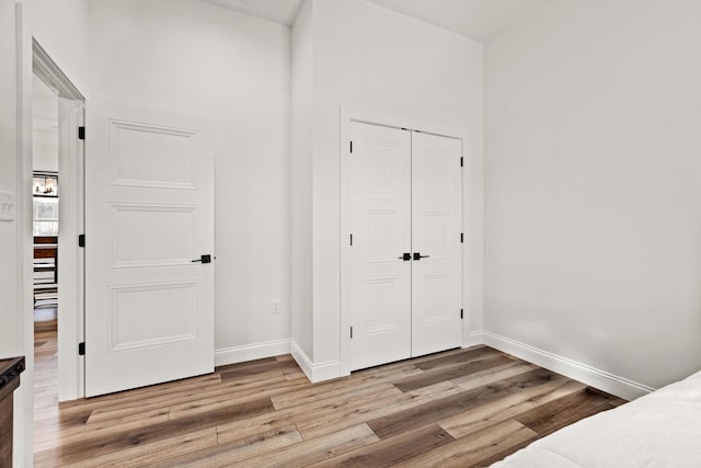 bedroom with light wood-type flooring, baseboards, and a closet