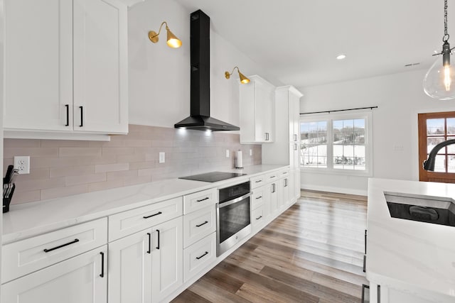 kitchen with white cabinets, light stone counters, oven, wall chimney range hood, and pendant lighting