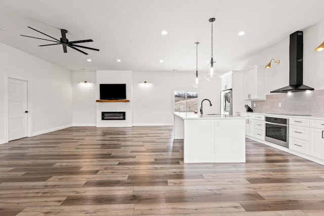 kitchen with a center island with sink, white cabinets, wall chimney exhaust hood, stainless steel appliances, and light countertops