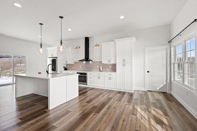 kitchen featuring appliances with stainless steel finishes, white cabinetry, wall chimney range hood, and an island with sink