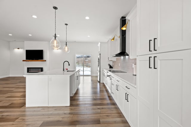 kitchen featuring light countertops, a kitchen island with sink, a sink, and wall chimney range hood