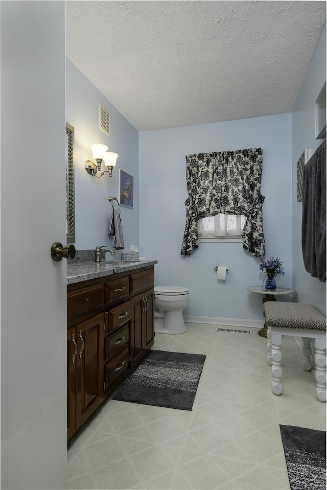 bathroom featuring a textured ceiling, toilet, vanity, and visible vents