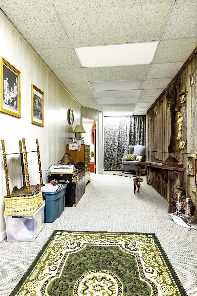 living area with wood walls, carpet, and a paneled ceiling