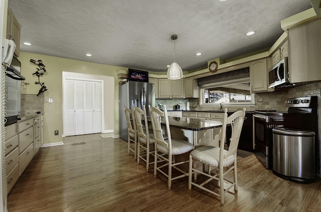 kitchen featuring baseboards, decorative backsplash, dark wood-style flooring, decorative light fixtures, and stainless steel appliances