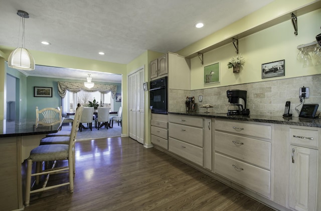 kitchen with tasteful backsplash, dark wood finished floors, oven, hanging light fixtures, and recessed lighting