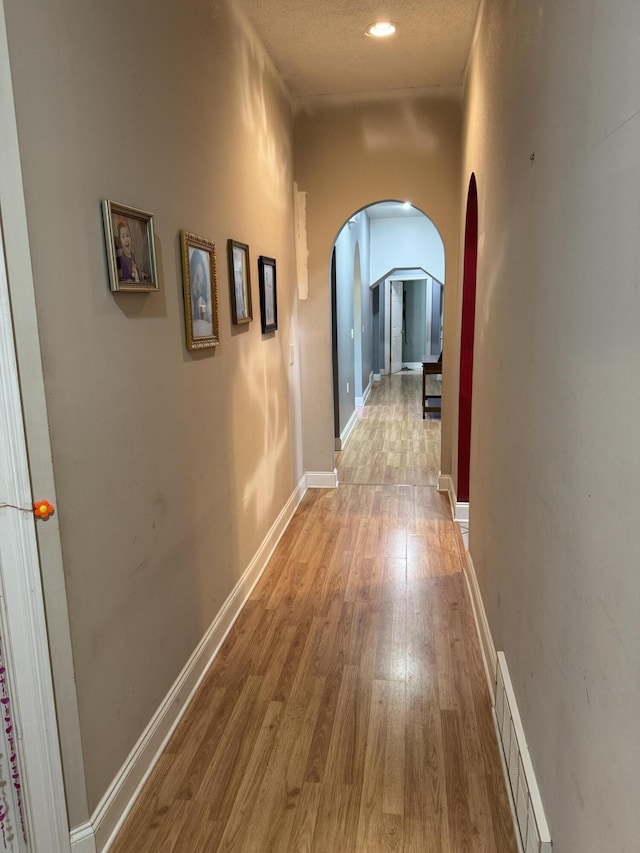 corridor with baseboards, recessed lighting, visible vents, arched walkways, and wood finished floors