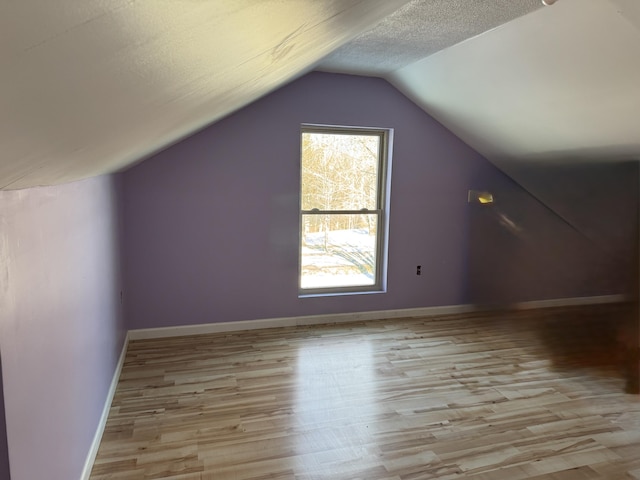 bonus room featuring light wood-type flooring, baseboards, a textured ceiling, and lofted ceiling