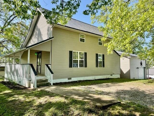 rear view of property with metal roof, covered porch, a yard, driveway, and crawl space