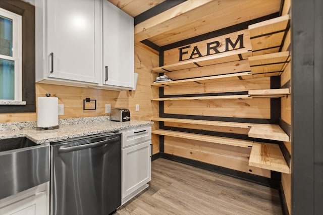 kitchen with open shelves, stainless steel dishwasher, white cabinetry, wooden walls, and light stone countertops