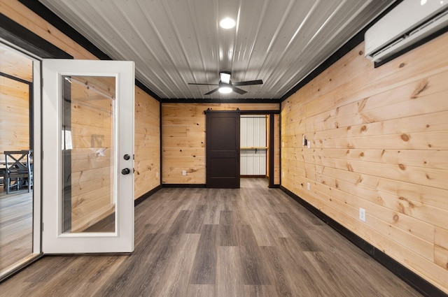 unfurnished room with dark wood-style floors, a barn door, a wall mounted AC, ceiling fan, and wooden walls