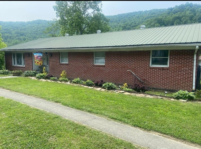 ranch-style house with metal roof, brick siding, a front lawn, and a wooded view