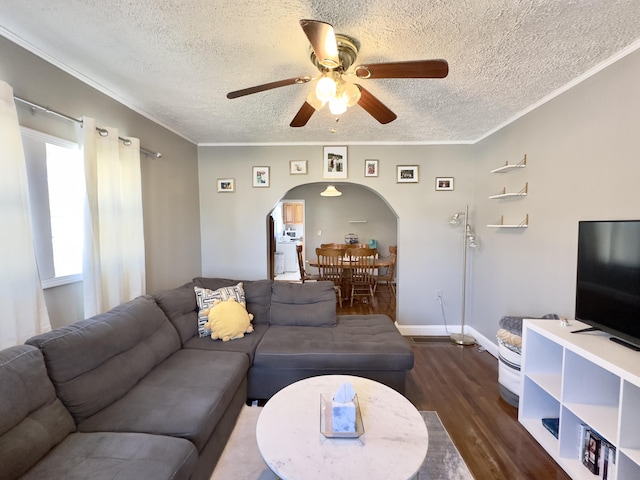 living room with dark wood-style floors, ceiling fan, arched walkways, and crown molding